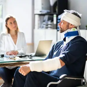 Man with head, neck, and arm injuries in a wheelchair, talking to a woman at a desk in an office - Lund Law Carolina