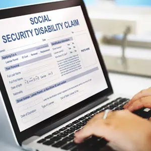 Hands typing on a laptop showing a Social Security Disability claim form on the screen. 